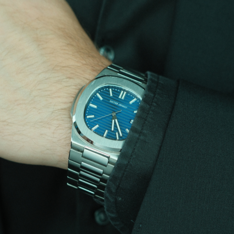 Close-up of a person wearing a silver watch with a blue face on a dark background